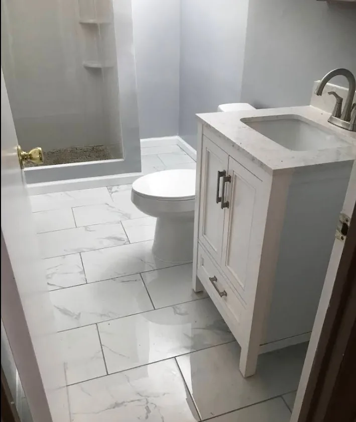 Bathroom renovation with white vanity, gold fixtures, and marble tile flooring