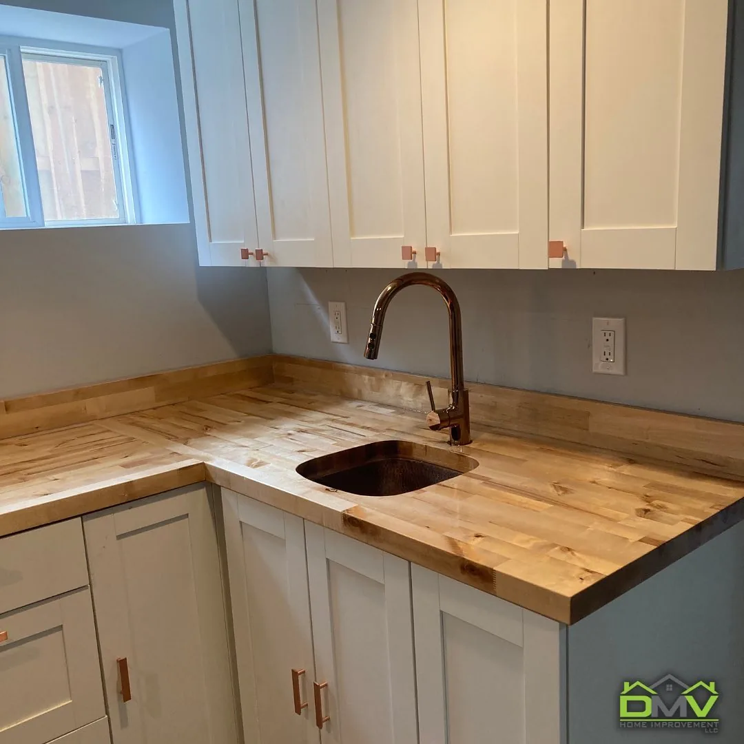 Kitchen with butcher block countertops, white shaker cabinets, and copper faucet